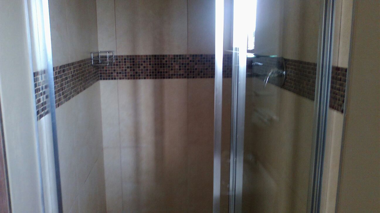 A glass-enclosed shower area with a tiled wall and a metal shelf.