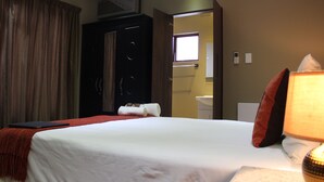 A hotel room with a bed, a desk, a lamp, a window, and a bathroom visible through an open door.