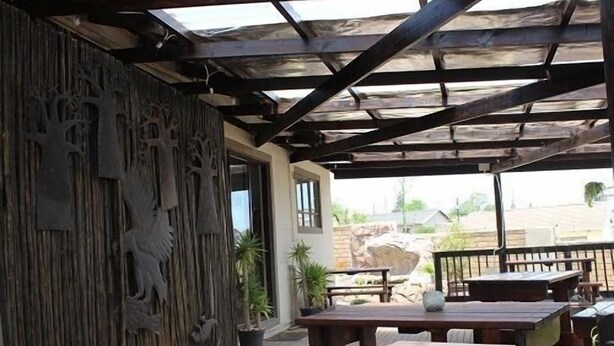 An outdoor patio with wooden tables and benches, a decorative wall with tree carvings, and a view of the surrounding landscape.