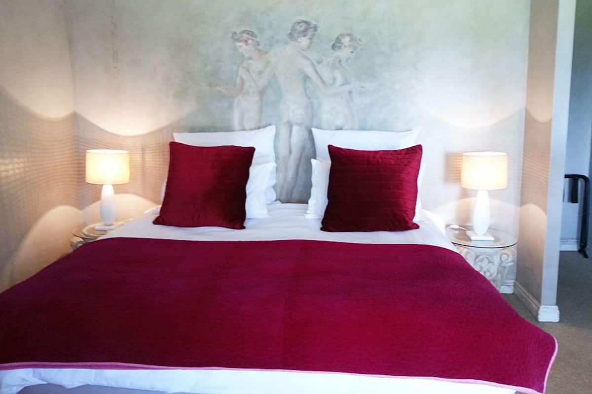 Una cama con manta y almohadas rojas, dos lámparas de noche y una pared con un mural.