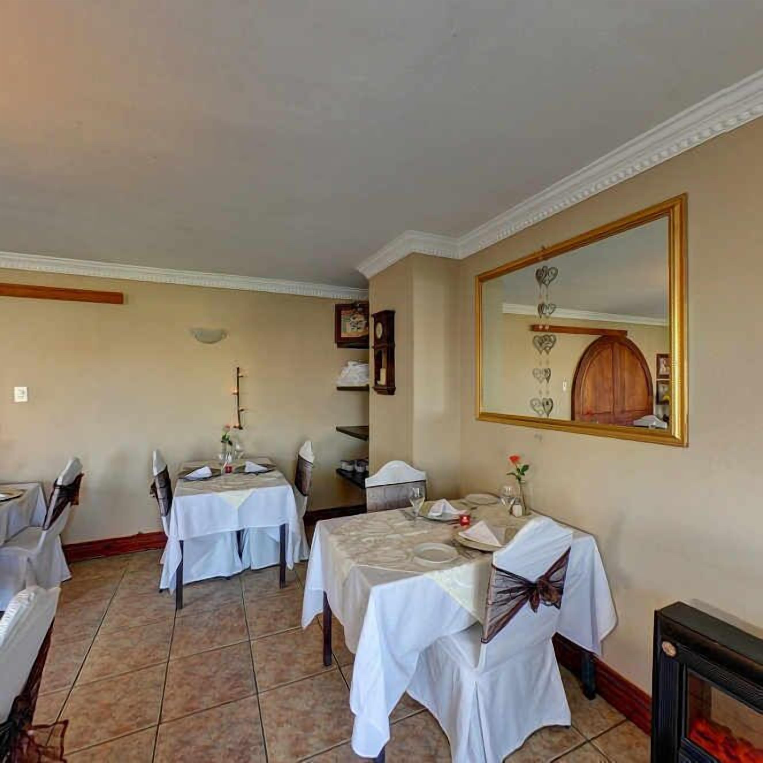 A dining area with two tables set for a meal, a large mirror on the wall, and a fireplace.