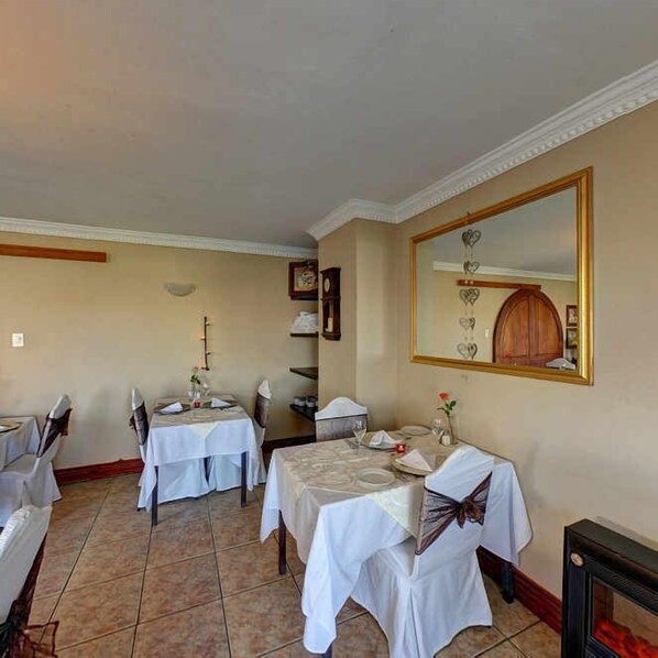 Un coin repas avec deux tables dressées pour le repas, un grand miroir au mur et une cheminée.