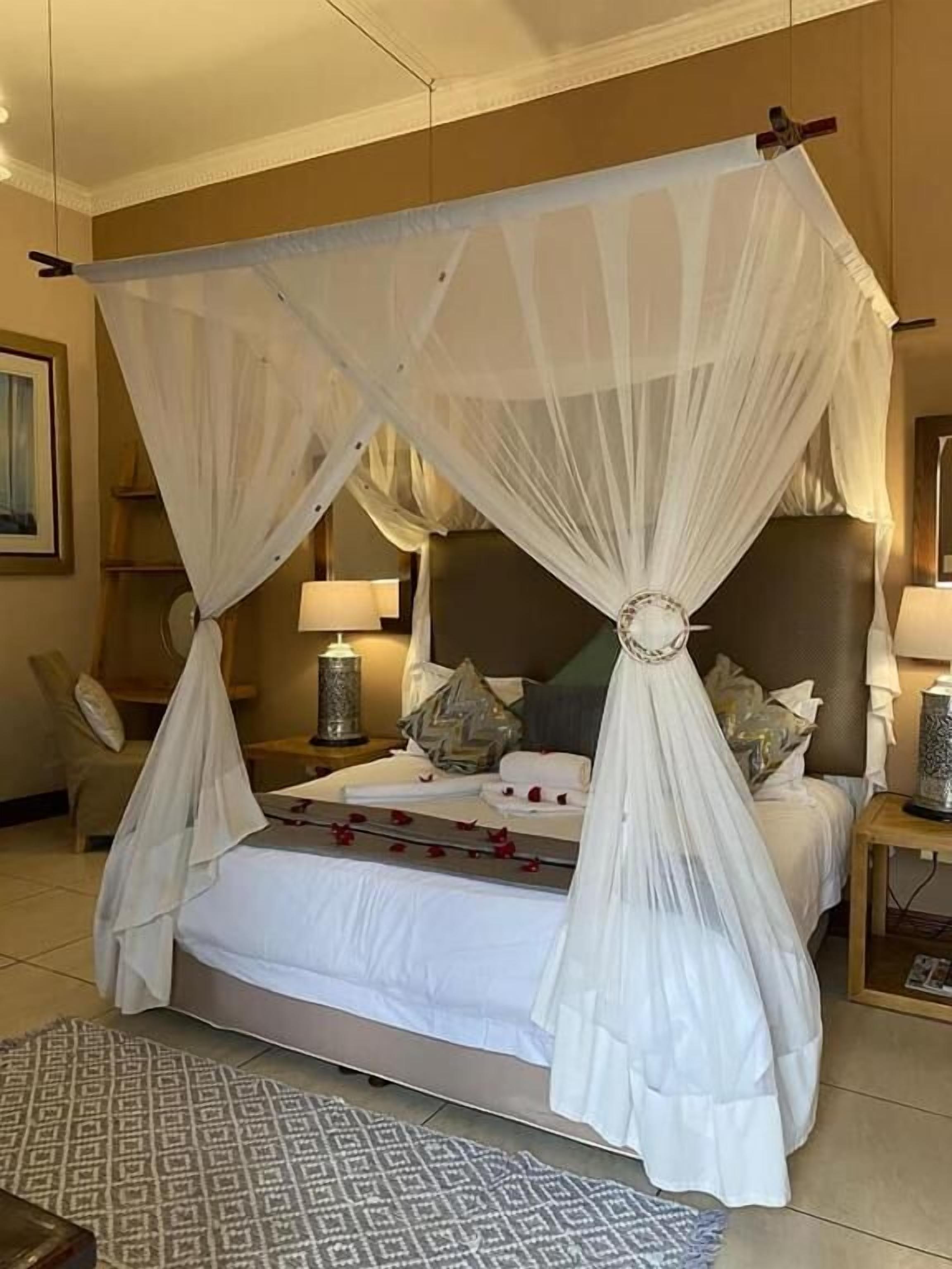 A four-poster canopy bed with a decorative centerpiece, bedside lamps, and a patterned rug.