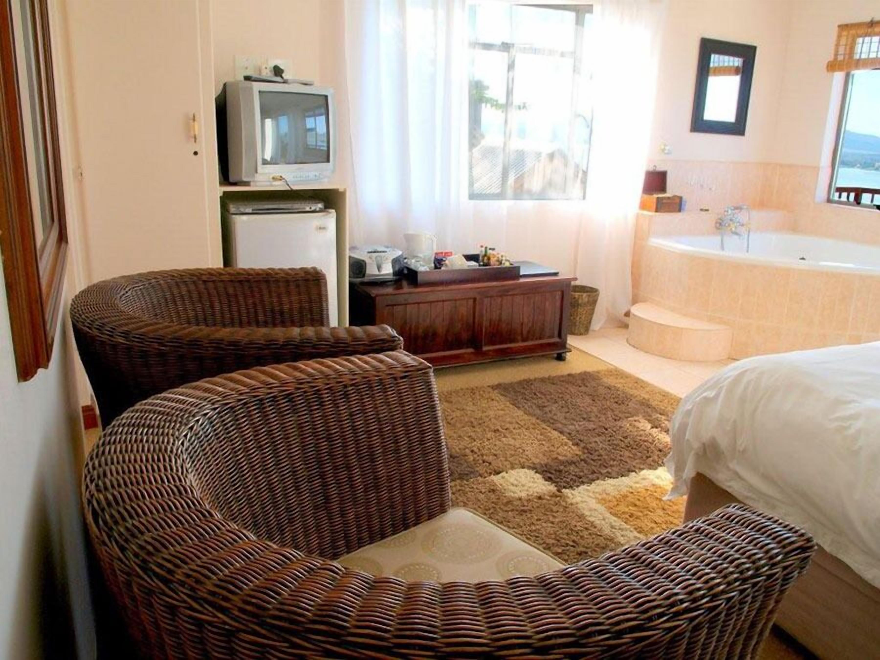 A hotel room with wicker furniture, a television, a desk, a bathtub, and a view of the outdoors.