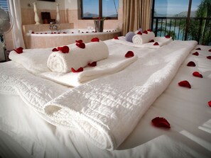 Une chambre d’hôtel avec un lit agrémenté de serviettes blanches et de pétales de rose, une baignoire et une vue sur la mer.