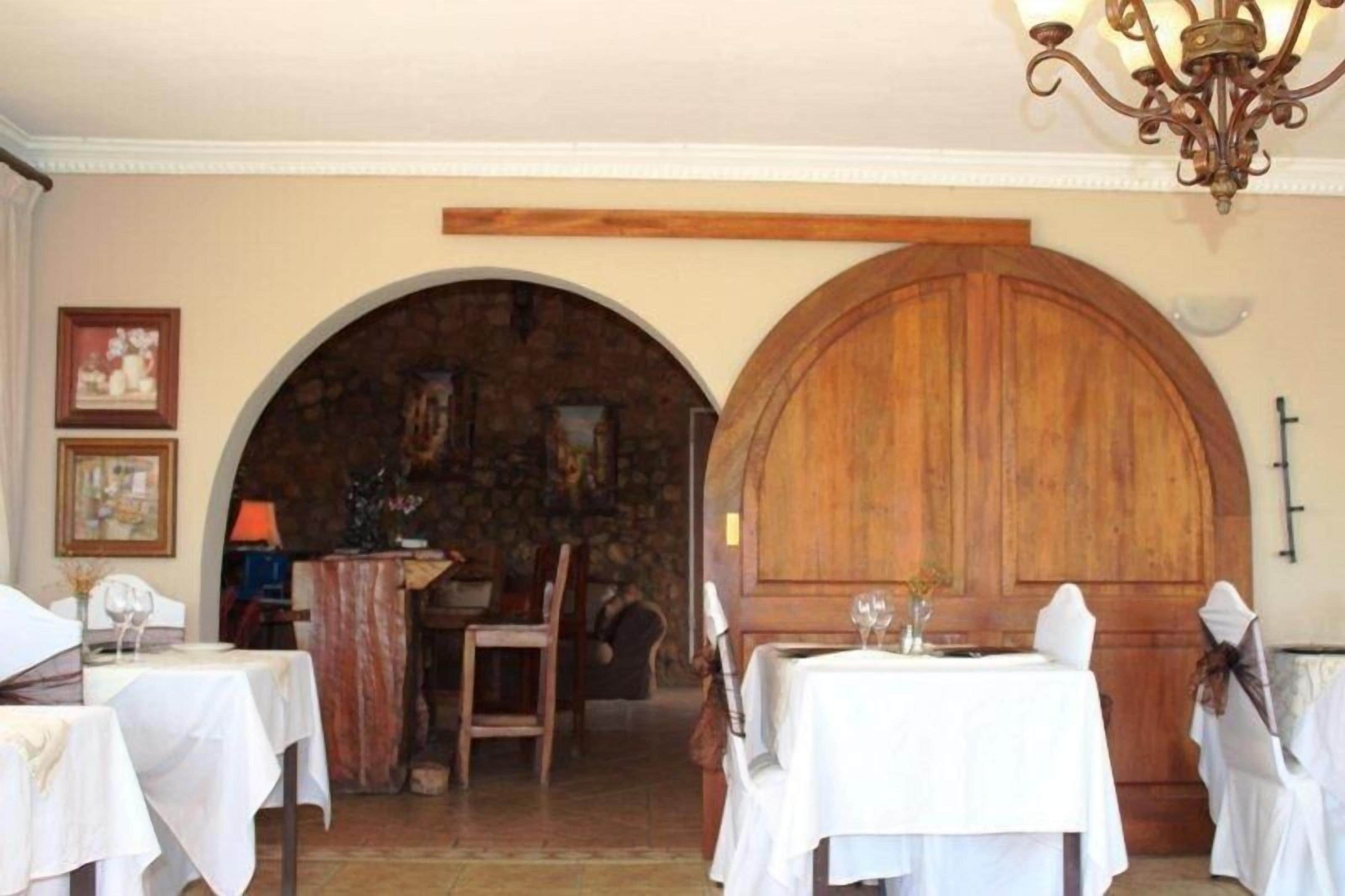 A dining area with tables set for two, a stone fireplace, and a wooden door.