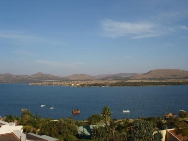 Vista costera con una masa de agua, barcos y colinas a la distancia.