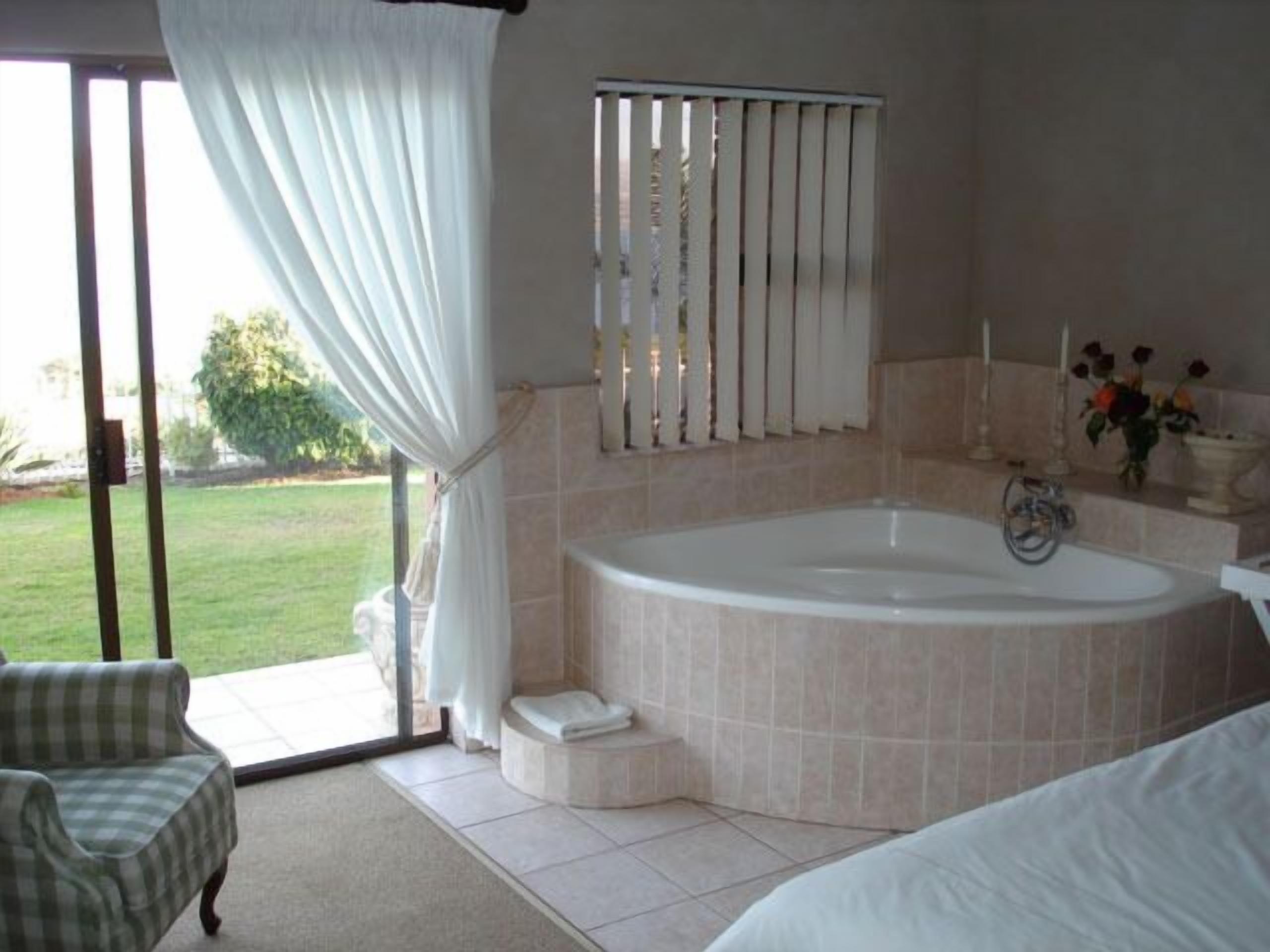 A bathroom with a large bathtub, a shower, and a toilet. There is a window with curtains, a sink, and a chair.