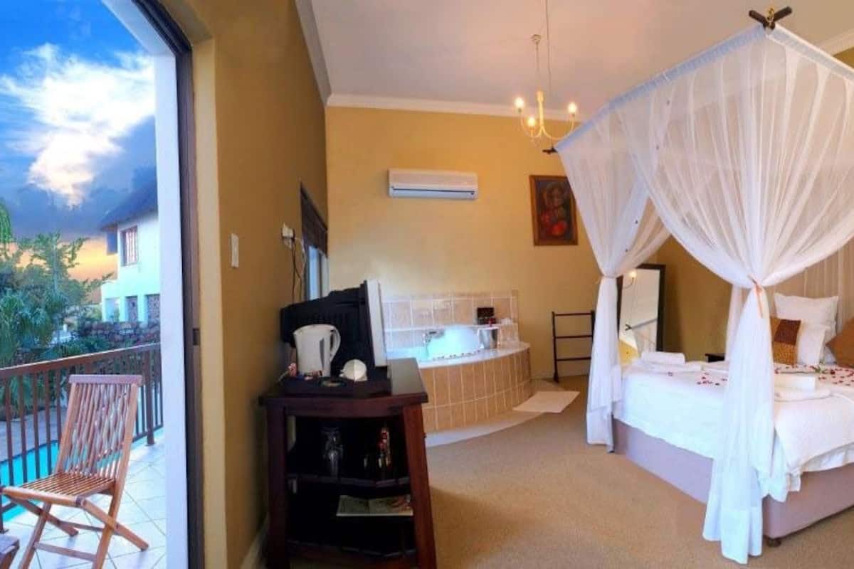 Un dormitorio con cama con dosel, un balcón con una silla y un baño con bañera.