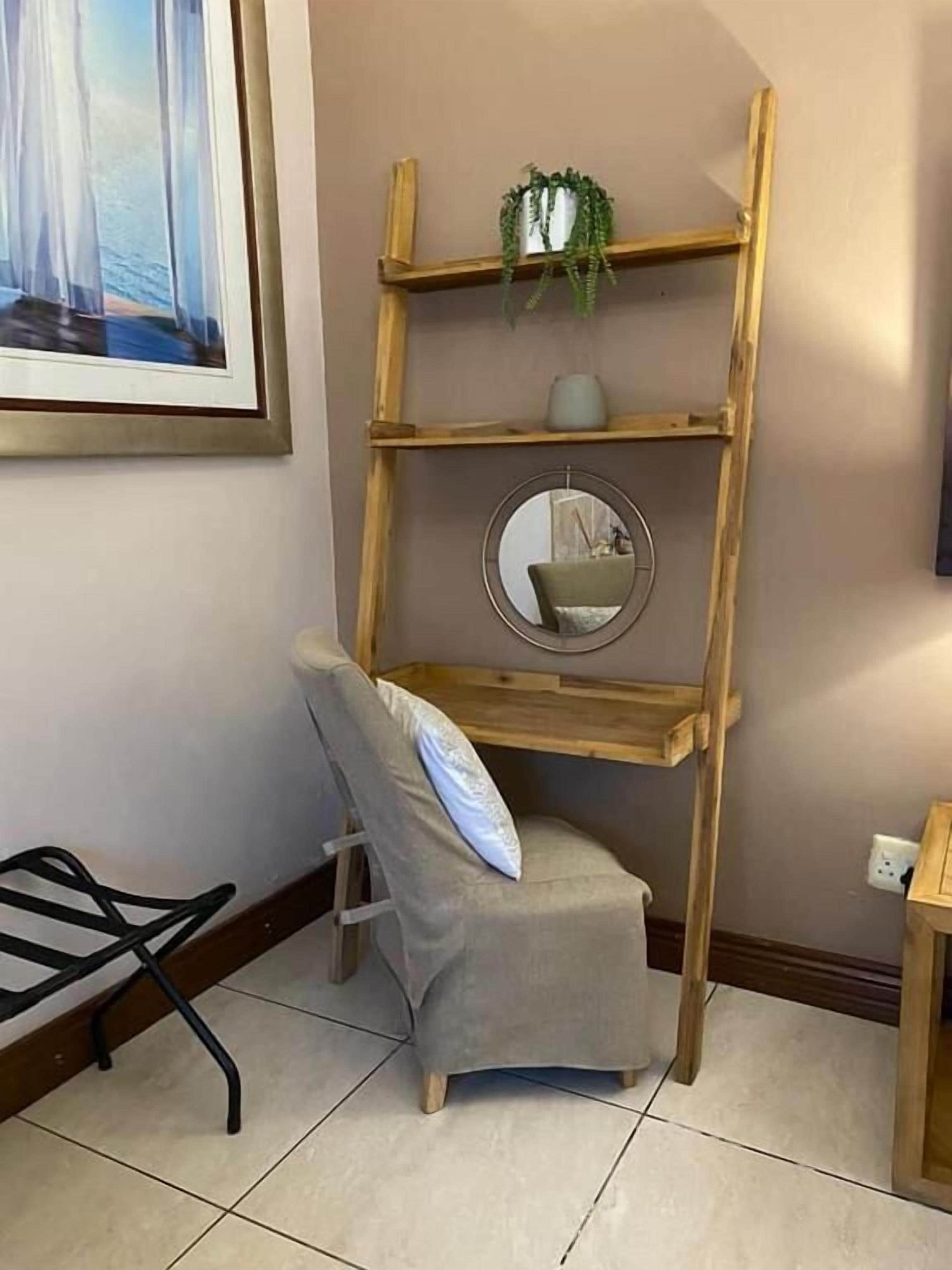A room with a wooden ladder shelf unit, a grey chair, and a framed picture on the wall.