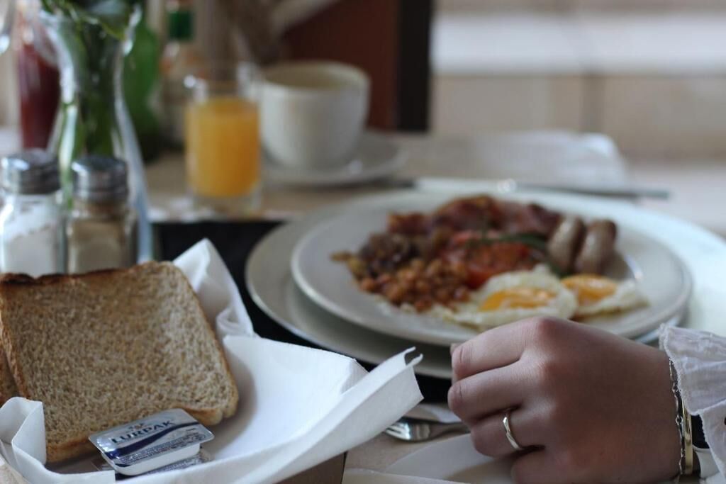 A breakfast setting with toast, scrambled eggs, and bacon on a plate, a glass of orange juice, and a cup of coffee on the table.