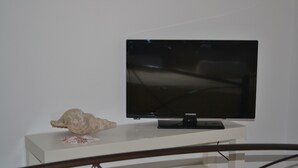 A flat-screen TV on a white stand with a decorative shell. - Floralia (Santorini)