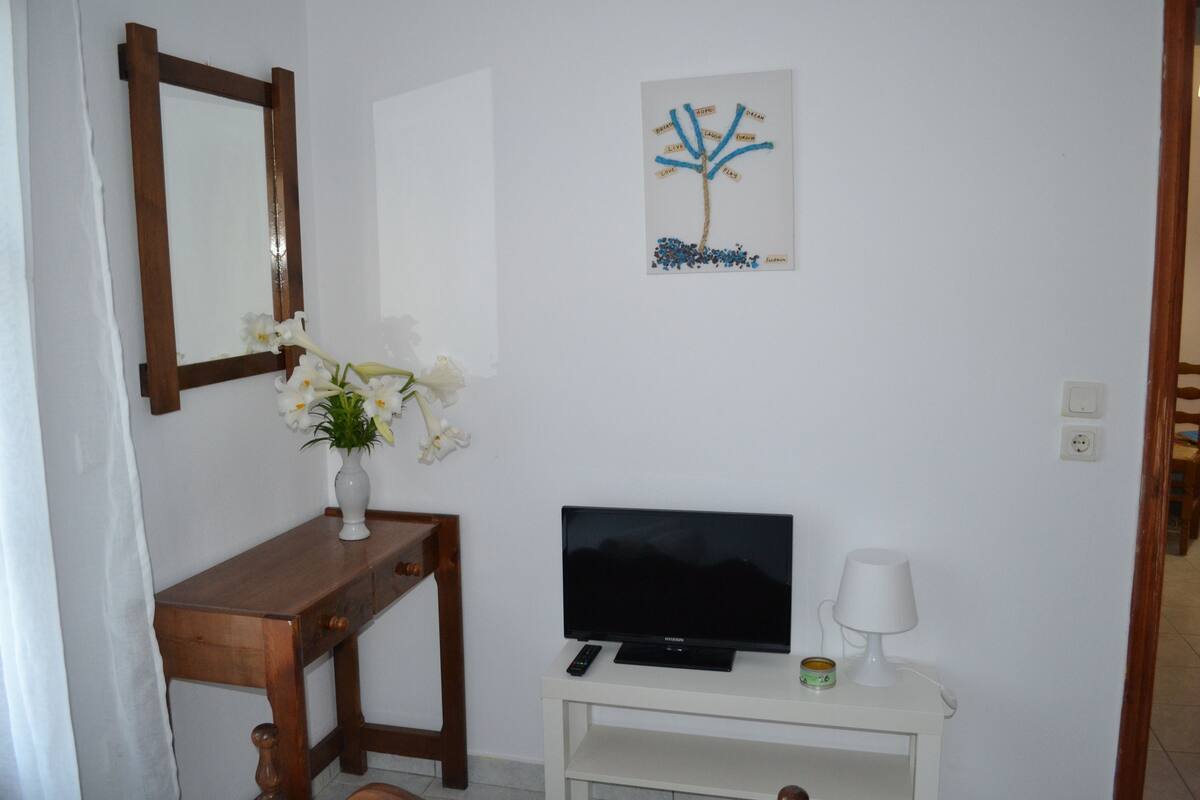 A room with a wooden desk, a television, a small white cabinet, and a wall-mounted picture.