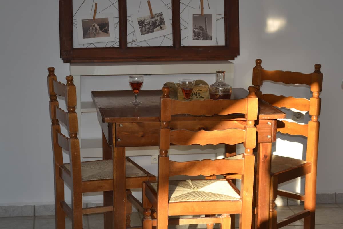 A wooden dining table with four chairs, a wine glass, and a bottle of liquor. Above the table, there is a framed picture with three photographs.