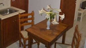 A kitchen with wooden cabinets, a sink, and a dining table with chairs. There is a vase with flowers on the table. - Floralia (Santorini)