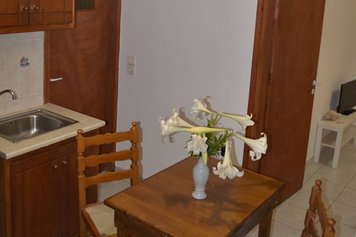 A kitchen with wooden cabinets, a sink, and a dining table with chairs. There is a vase with flowers on the table.