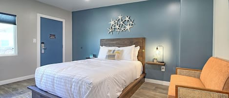 A bedroom with a bed, a chair, a nightstand, and a wall decoration.