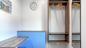 A room with a blue accent wall, a wooden table with benches, a clock, a coat rack, and a mirror. - White Caps Motel (Ventura)