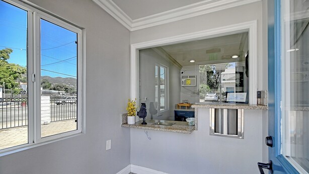 A bathroom with a large window, a countertop with a sink, and a mirror. - White Caps Motel (Ventura)