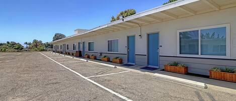 A row of single-story motel rooms with individual doorways, a covered parking area, and small planters along the building's exterior.