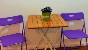Ein kleiner Raum mit einem Holztisch und zwei violetten Stühlen. Darüber hängt an der Wand ein gerahmtes abstraktes Gemälde.