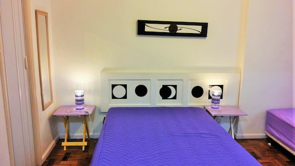 A bedroom with a bed, two bedside tables, a nightstand, a wall-mounted lamp, and a framed picture above the bed.