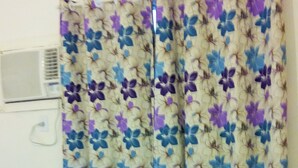 Ein Zimmer mit einem violetten Sofa, einer weißen Klimaanlage und blumigen Vorhängen.