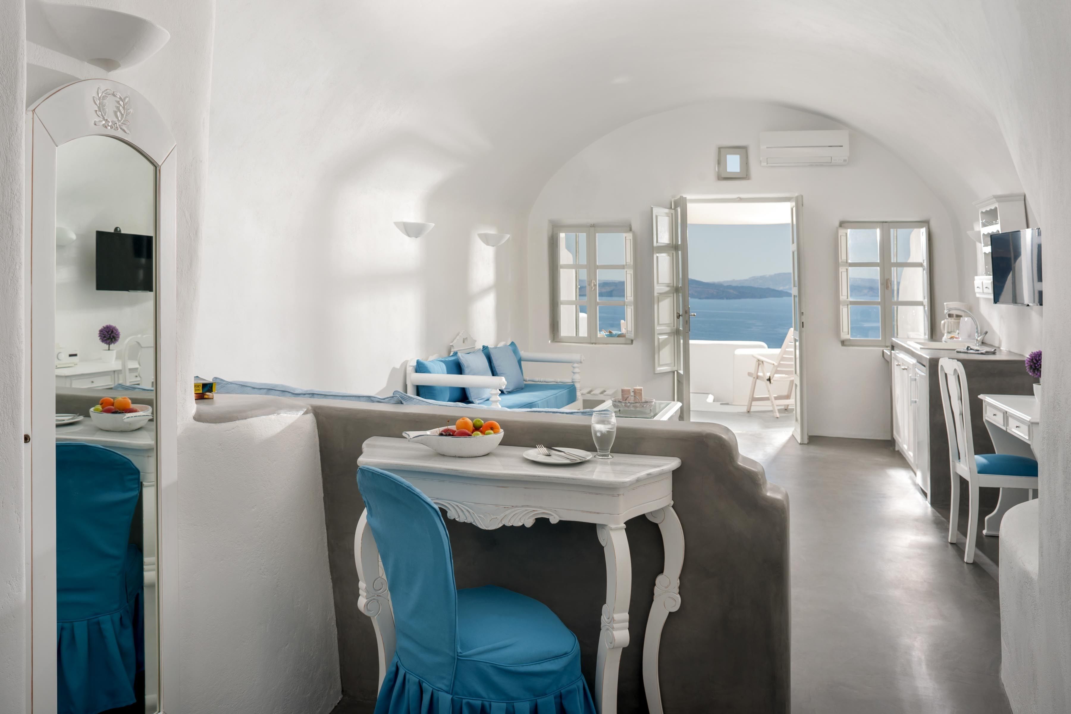 A bright, white interior with a dining area, a sofa, and a view of the sea.