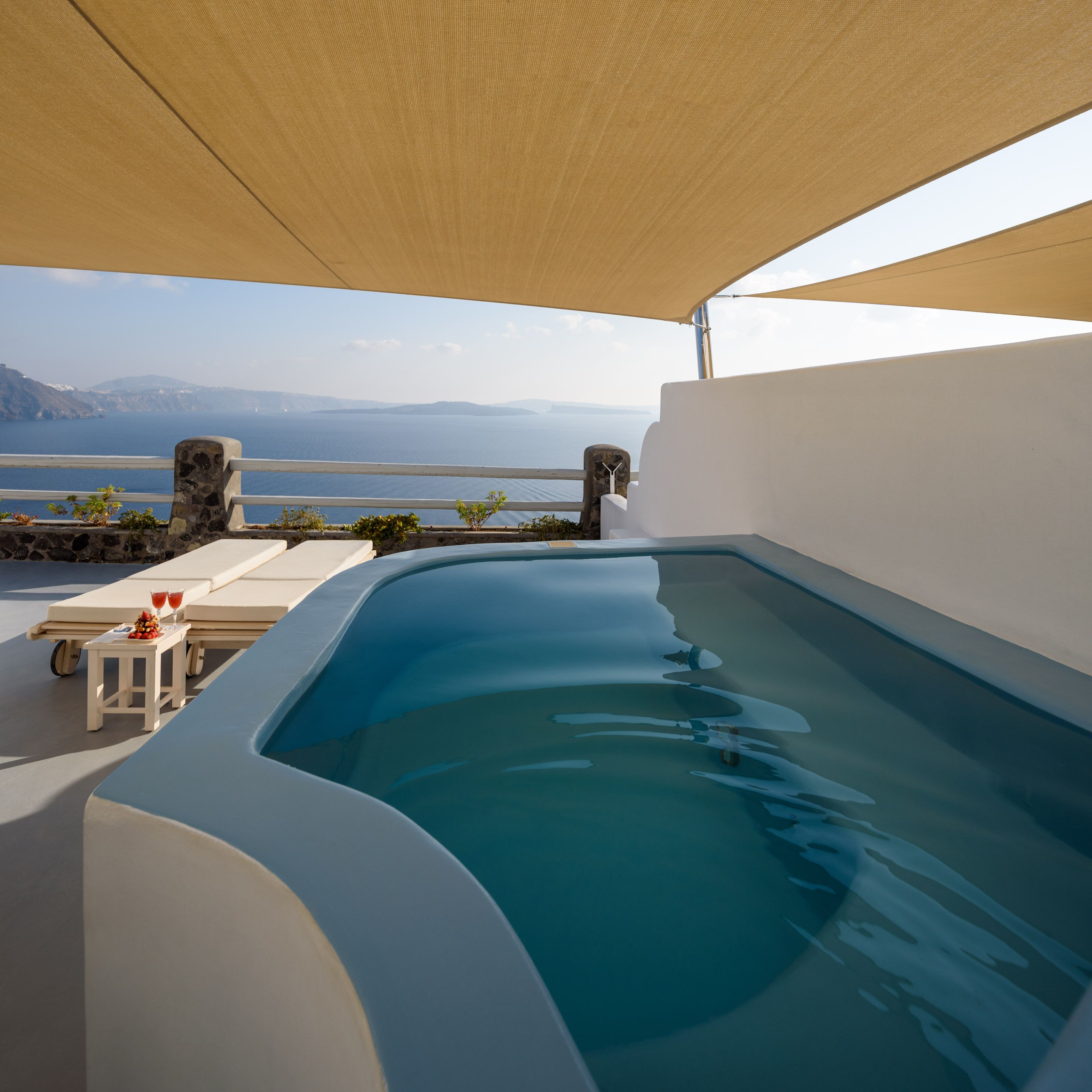 A swimming pool with a view of the sea, a sun lounger, and a small table with drinks.