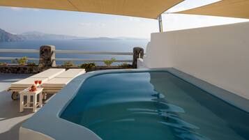 A swimming pool with a view of the sea, a sun lounger, and a small table with drinks.
