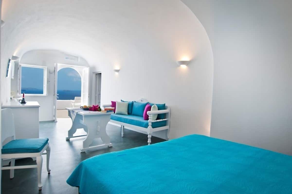 A room with a bed, a white sofa, a table, and a view of the sea.