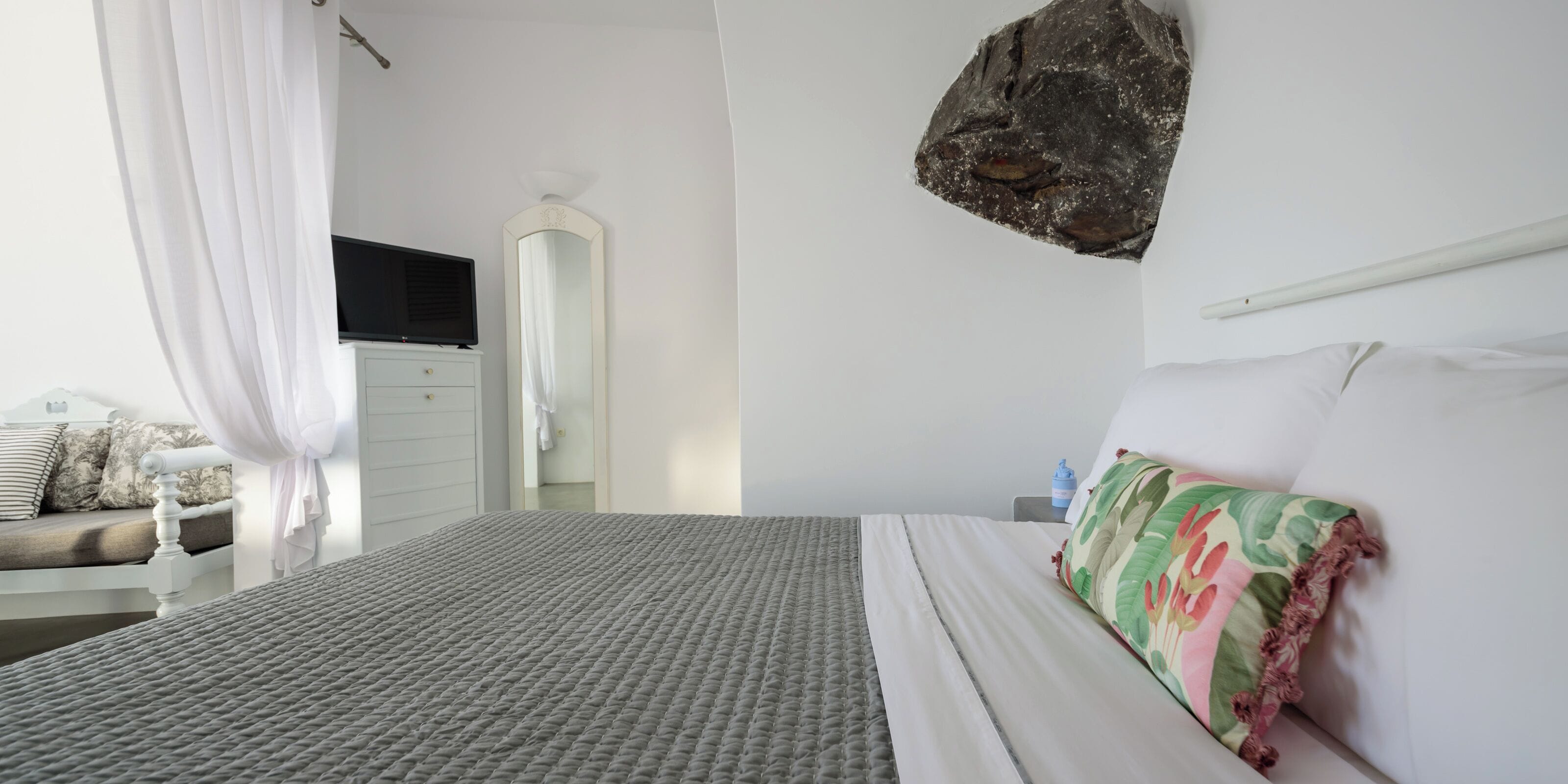 A bedroom with a bed, a TV, a mirror, and a large rock on the wall.