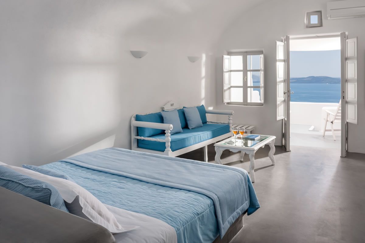 A bedroom with a bed, a sofa, a table with drinks, and a view of the sea.