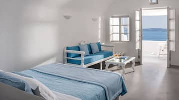 A bedroom with a bed, a sofa, a table with drinks, and a view of the sea.