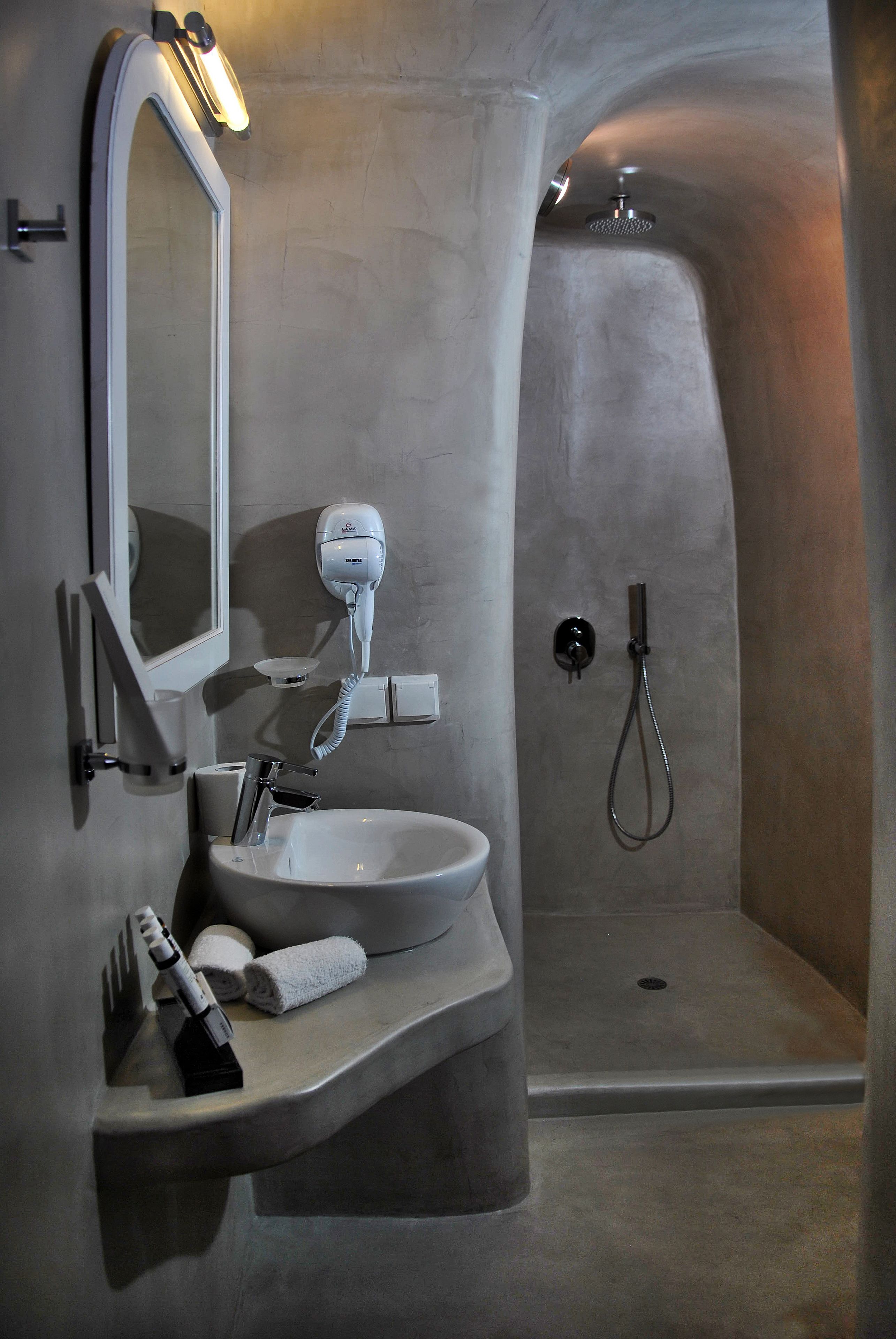 A modern bathroom with a built-in sink, a large mirror, a hairdryer, and a shower area.