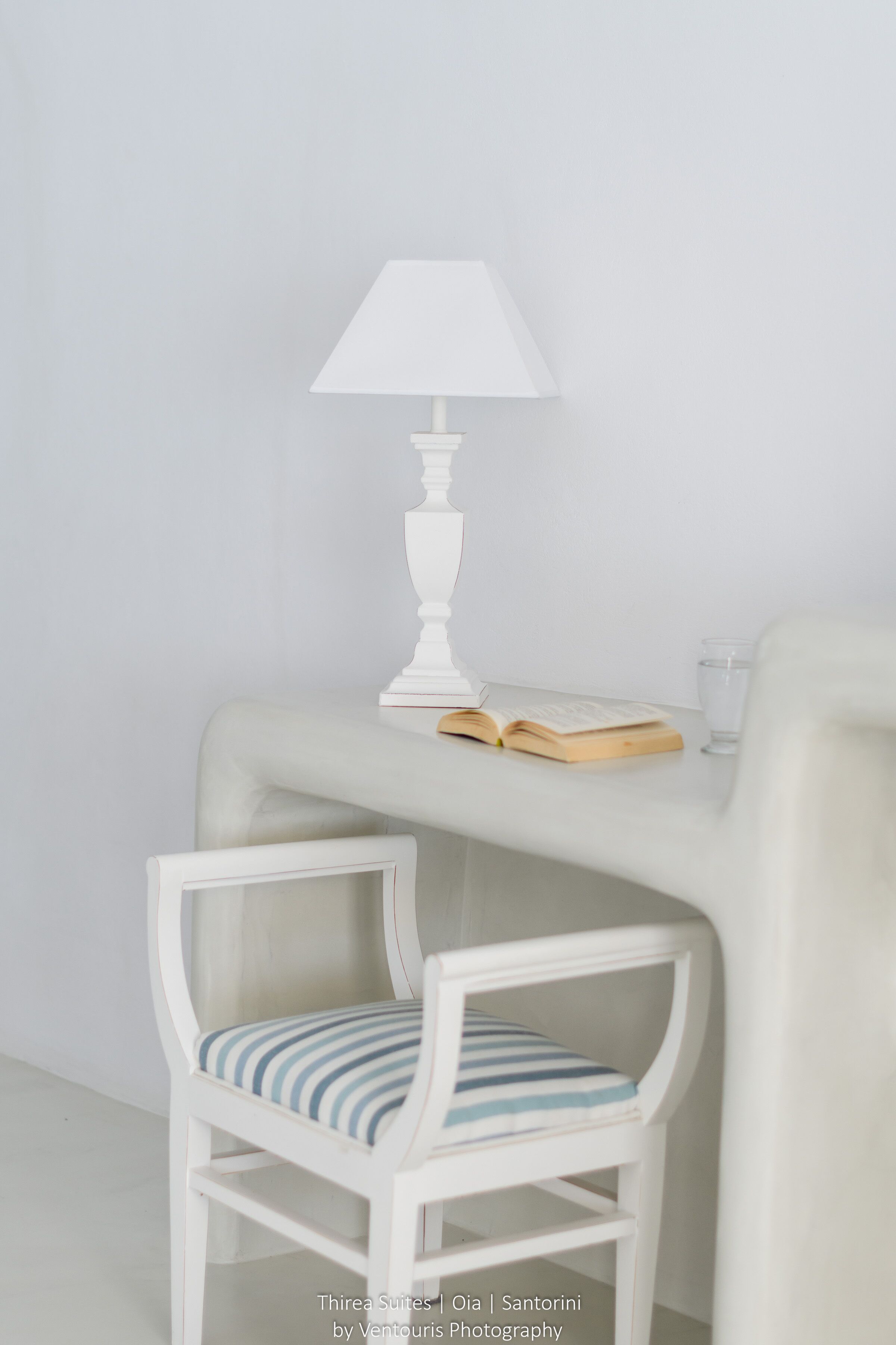 A white chair with a striped cushion, a white table with a lamp, and an open book.