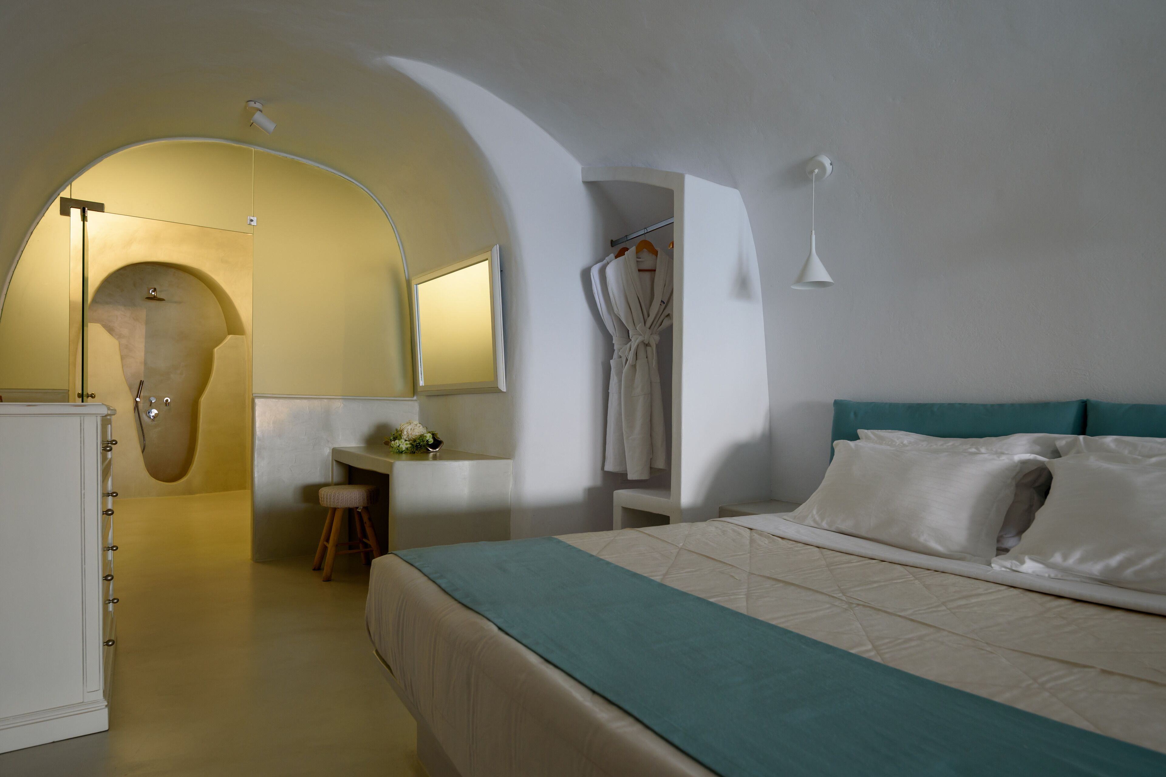 Una habitación de hotel con cama, escritorio, silla, bata y espejo.