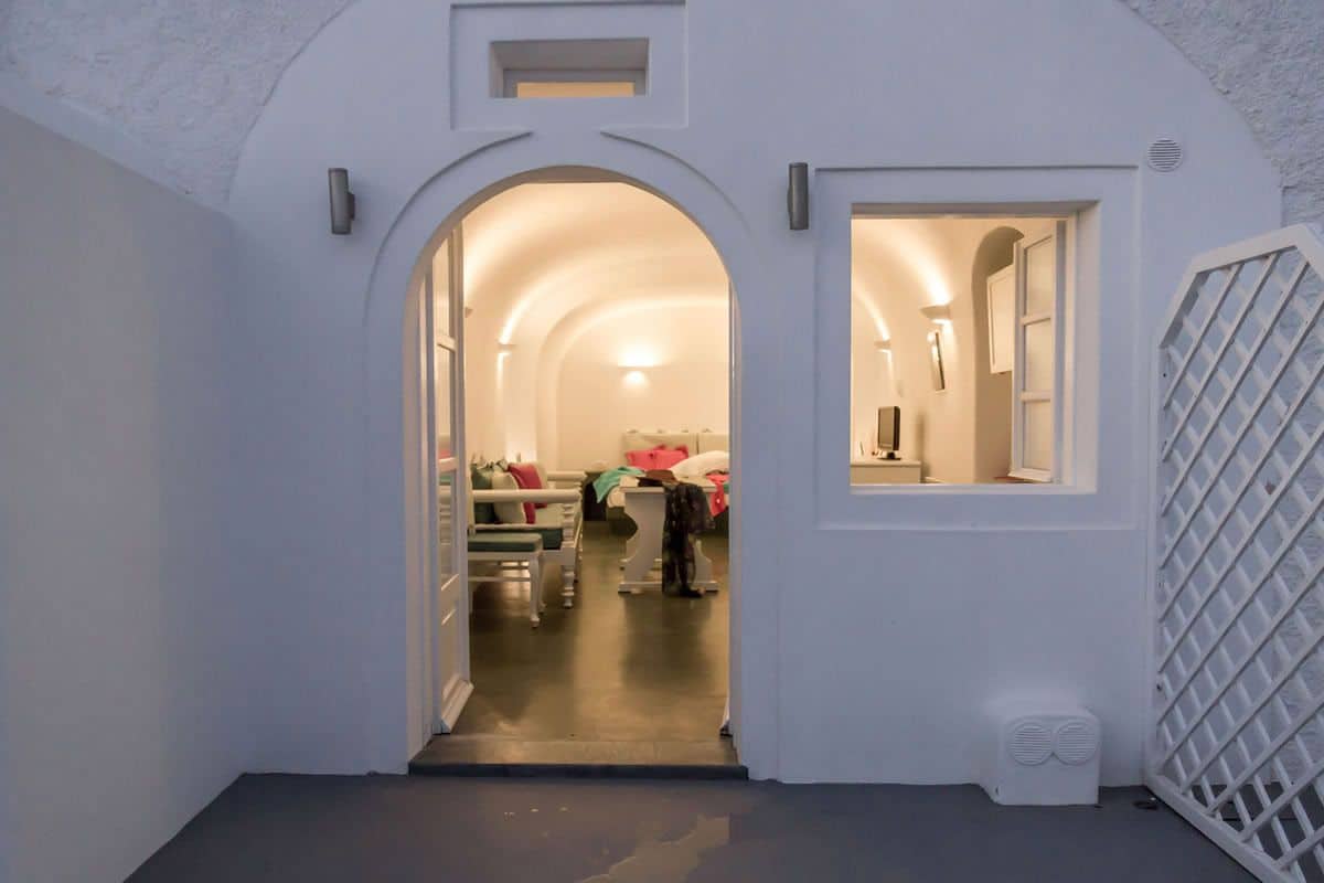 A narrow hallway with an arched doorway leading to a room with a bed and a bedside table.