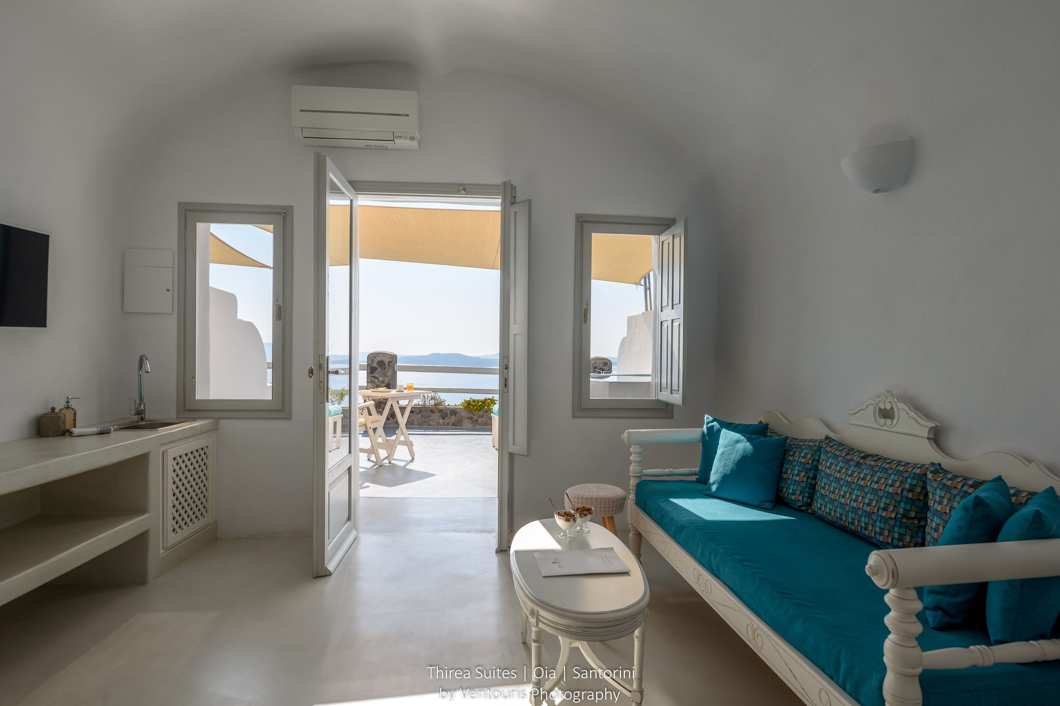 A room with a bed, a small table, a sofa, and a view of the sea.