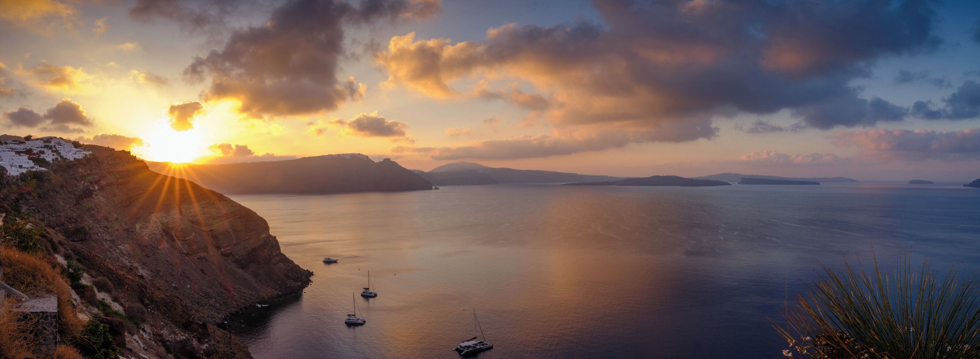 A coastal landscape with a sunset, calm sea, and boats.