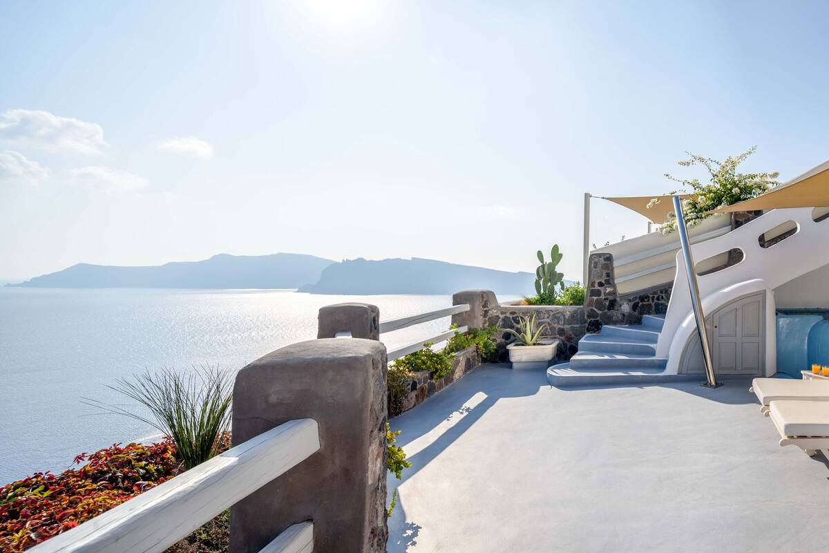 A sunlit outdoor area with a pool, lounge chairs, and a view of the sea.