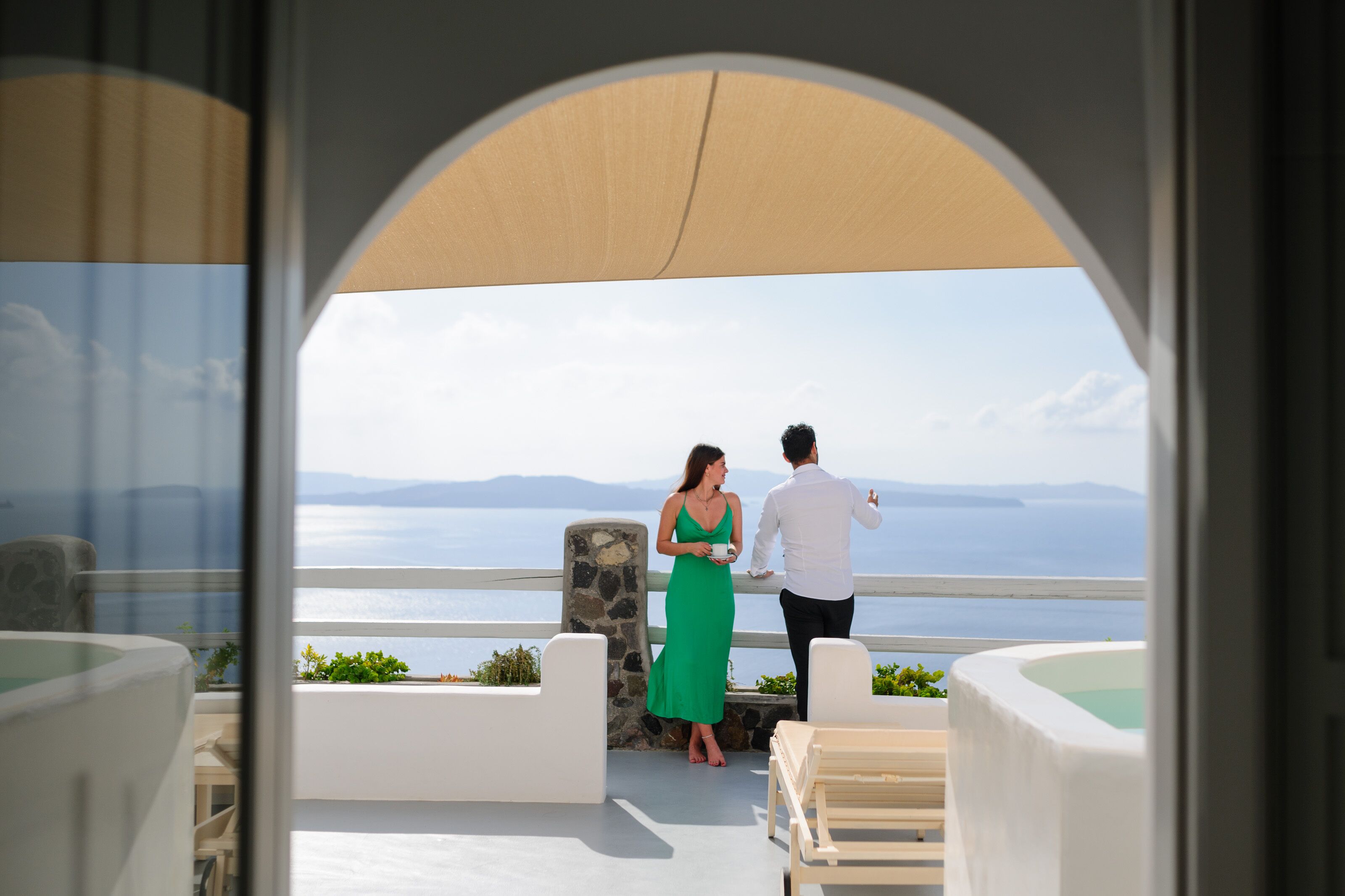 A couple on a balcony overlooking a scenic view of the sea and mountains.