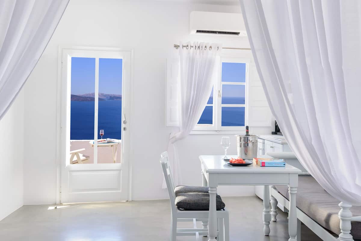 A room with a bed, a table with a wine bottle, and a view of the sea through a door.