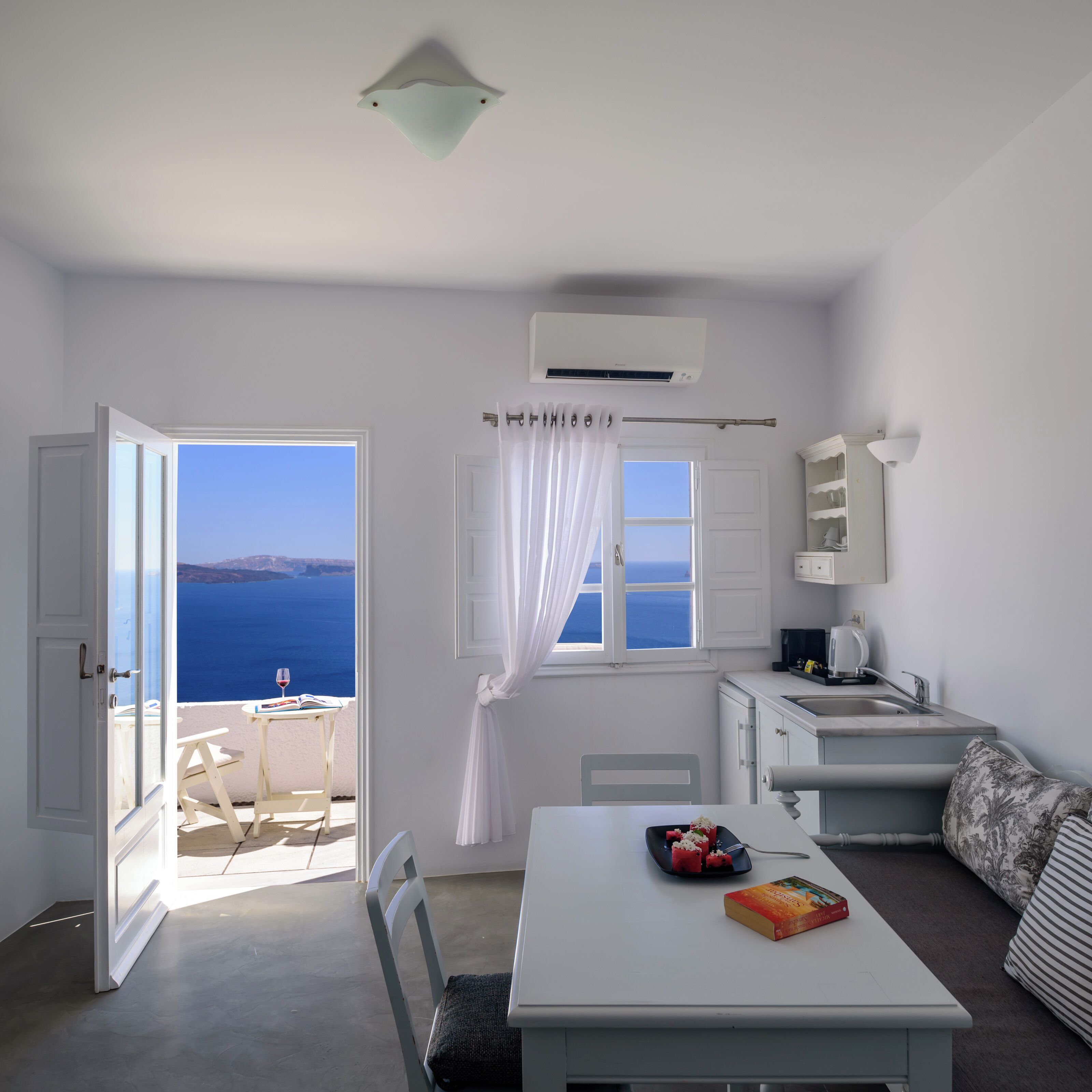 Une chambre avec vue sur la mer, une table à manger avec un livre et une assiette de nourriture, un climatiseur blanc et une petite kitchenette.