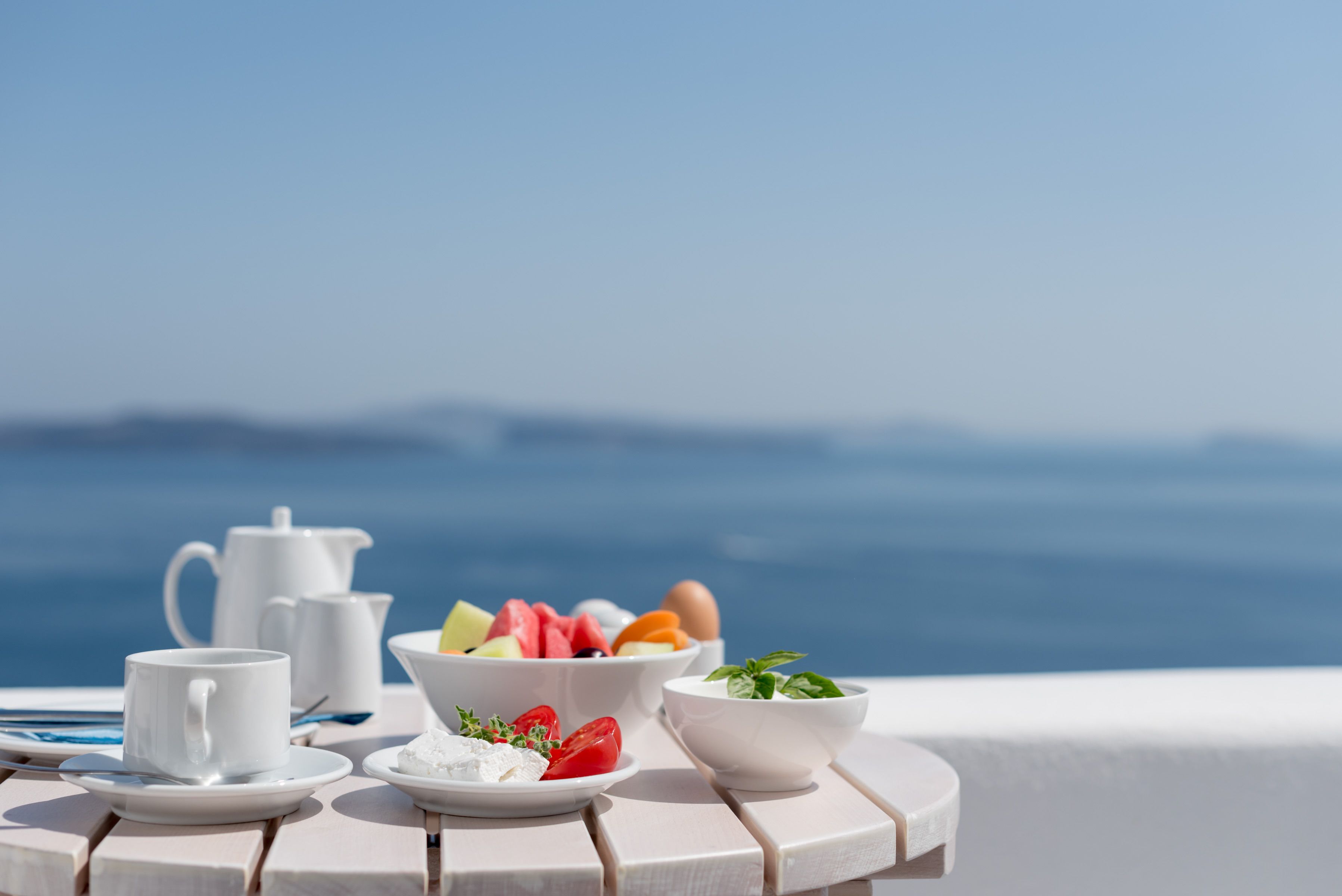 Une table dressée avec une théière blanche, des tasses et des bols remplis de fruits et de yaourt, offrant une vue panoramique.