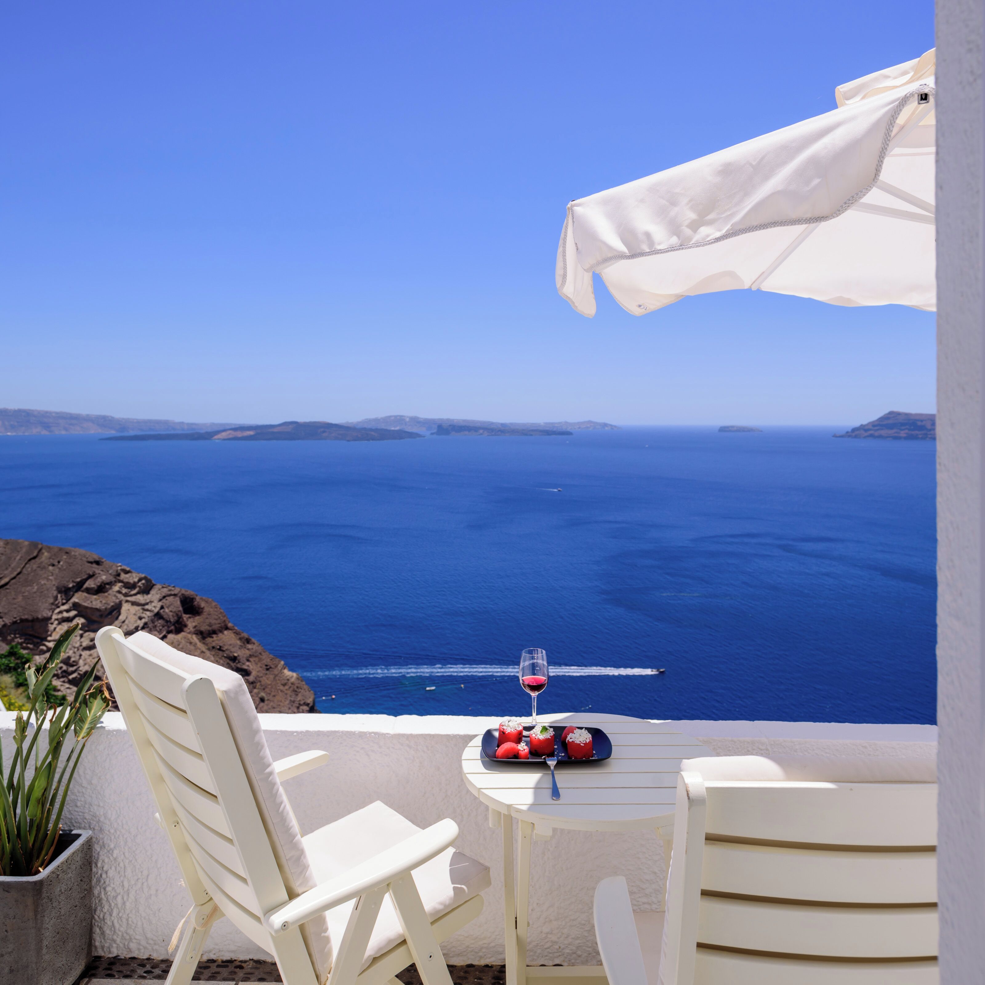 Un área de estar al aire libre con mesa y sillas, con vista al mar azul y la costa distante.