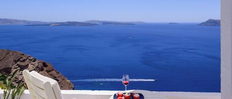 Un área de estar al aire libre con mesa y sillas, con vista al mar azul y la costa distante.