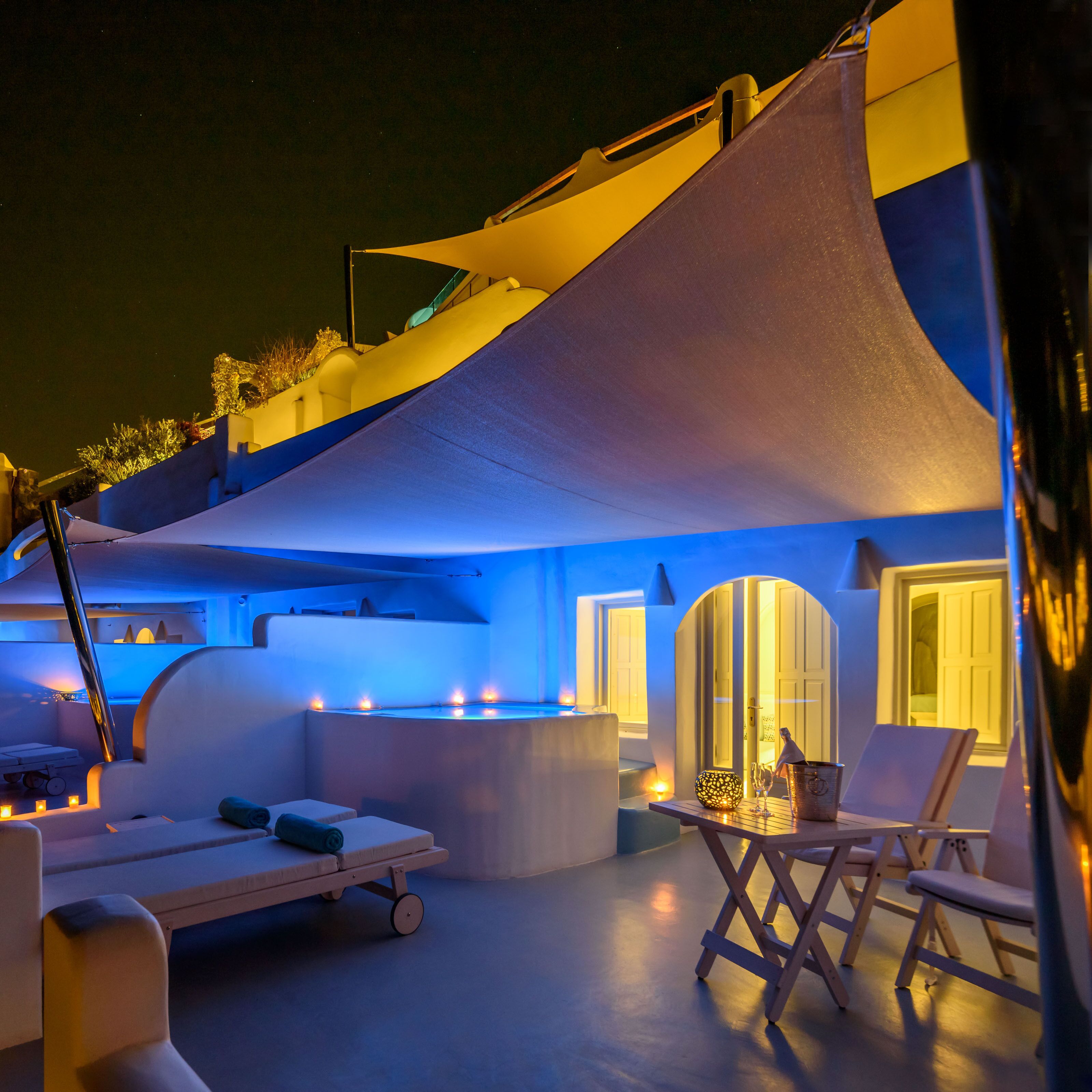 A modern outdoor lounge area with a canopy, lounge chairs, a bar area, and a pool.