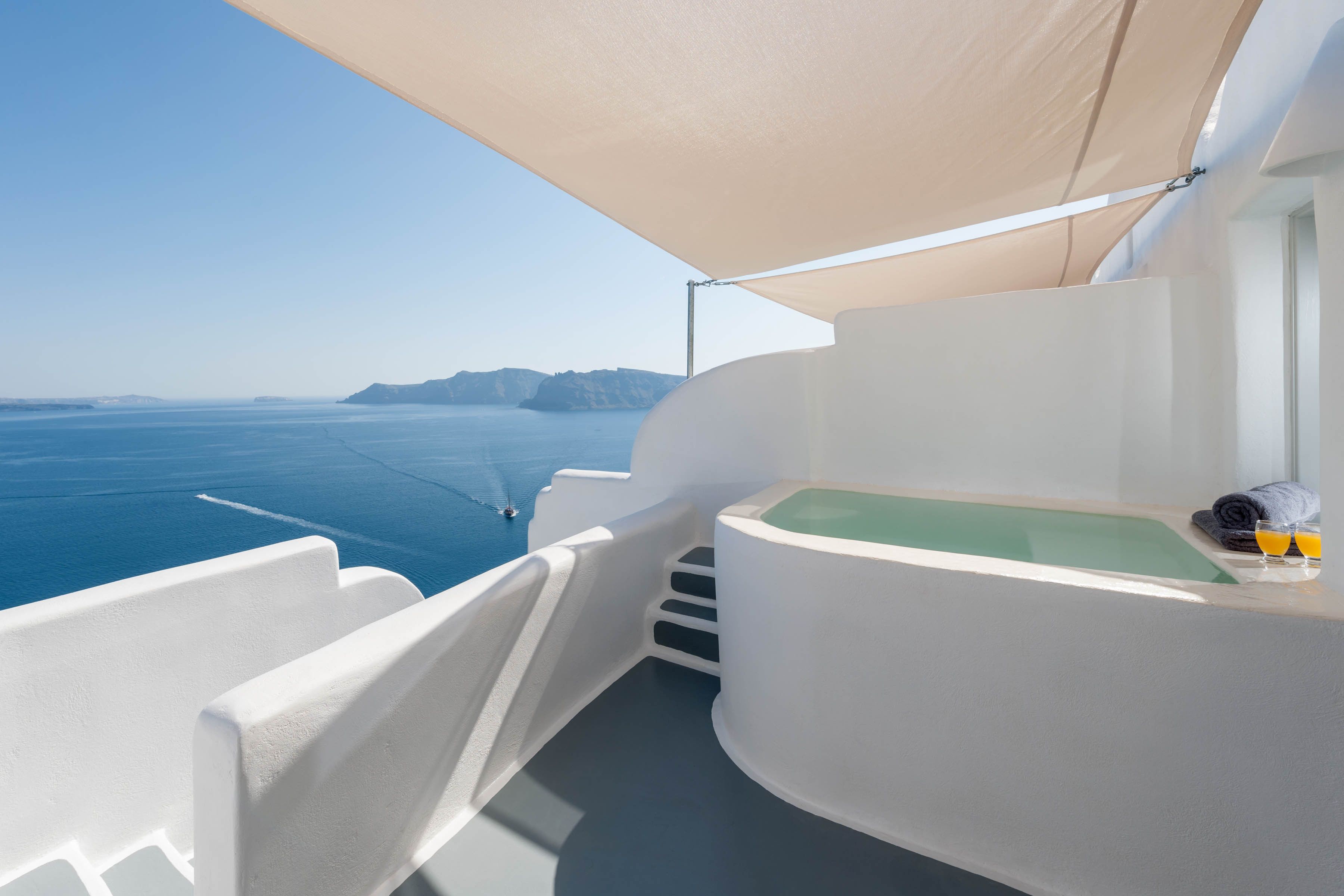 Un balcón con una bañera blanca, un toldo y vista al mar.