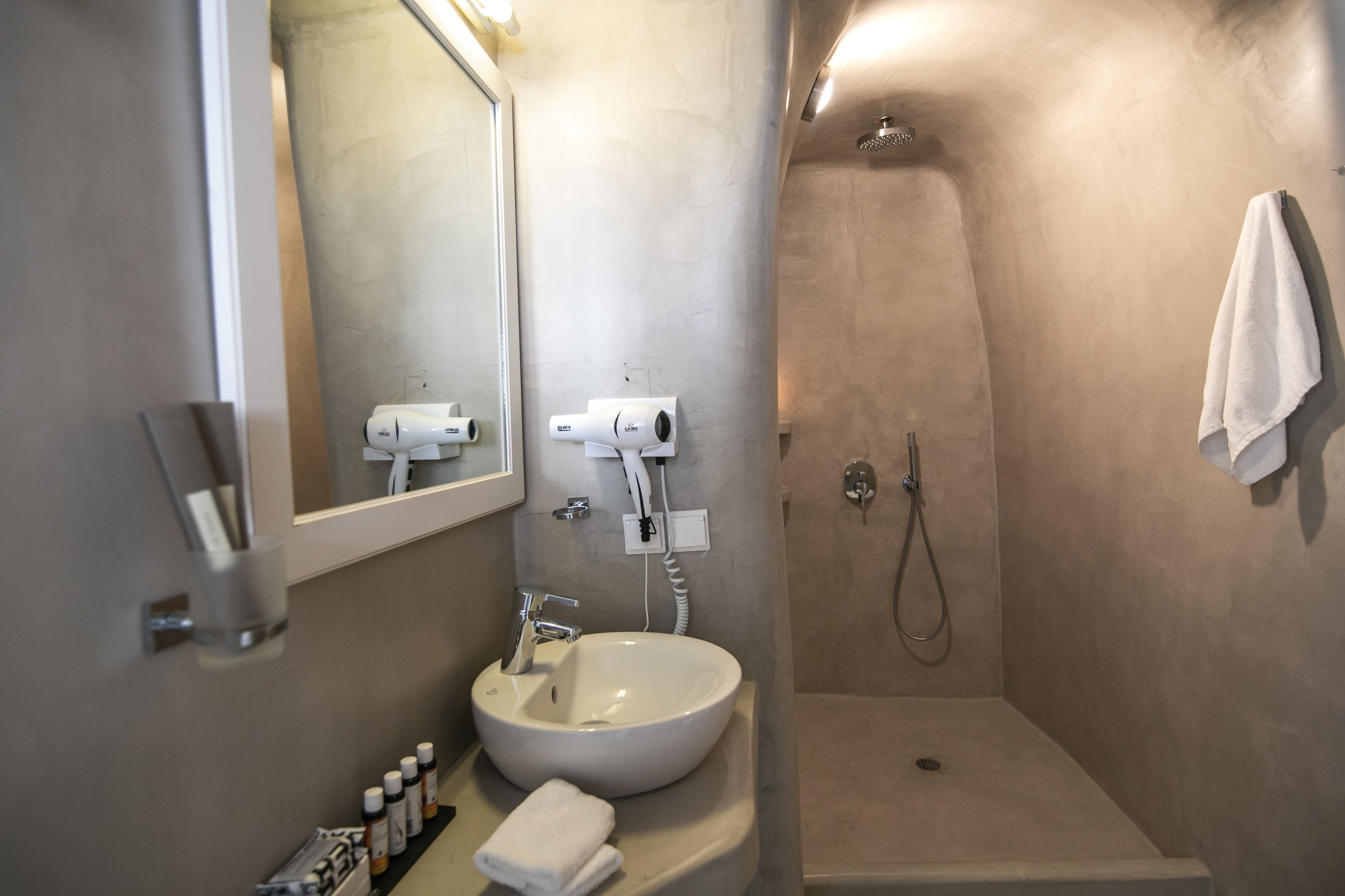 A modern bathroom with a white sink, a mirror, a hairdryer, and a shower.
